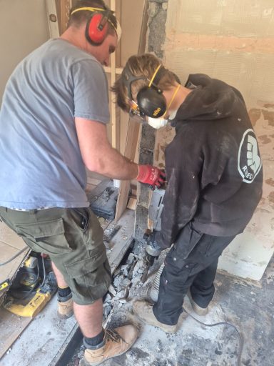 Oakmoor AP student using a power breaker to clear floor space for new plumbing installations.