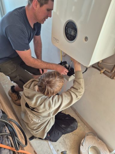 Close-up of an Oakmoor AP student using a screwdriver to adjust the electrical control interface of a wall-mounted boiler.