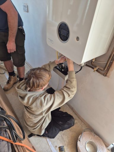 Student at Oakmoor AP working on the internal wiring and control panel of a modern combi-boiler under supervision.